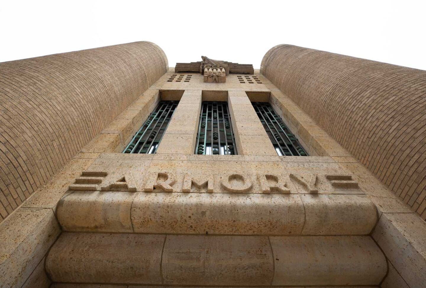 Low-angle view of a stone building facade with tall columns, vertical barred windows, an eagle sculpture, and the word “ARMORY” engraved above the entrance.